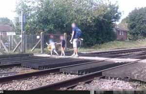 S Um jovem pai foi retratado andando com dois filhos do outro lado dos trilhos enquanto completamente distraído pelo telefone