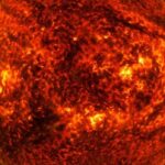 Um flare solar é visto em close, com um meio de material claro que se afasta de uma grande bola laranja e preta.