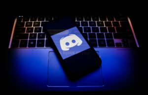 Discord lançará verificação de idade no próximo mês para acesso total à sua plataforma Discord logo displayed on a phone screen and a keyboard.