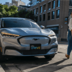 Woman walks up to silver Mustang Mach-E. License plate says "Ford Drive"