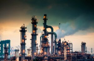 O novo fundo de US $ 800 milhões da ARA Partners ajudará a descarbonizar ativos industriais A steaming, glowing mass of smoke stacks and distillation towers connected by conduit and pipe racks towers in the early morning light in front of the Port of Los Angeles.