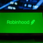 A Robinhood logo seen displayed on a smartphone with the stock market graphic in the background.