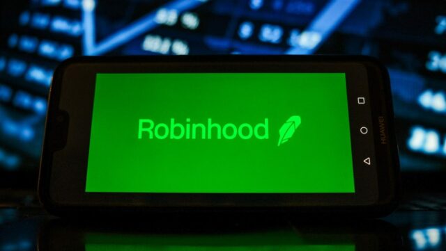 A Robinhood logo seen displayed on a smartphone with the stock market graphic in the background.