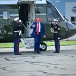 Donald Trump deixa o helicóptero, cercado por dois fuzileiros navais de uniforme.