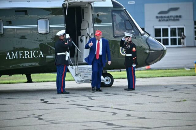 Donald Trump deixa o helicóptero, cercado por dois fuzileiros navais de uniforme.
