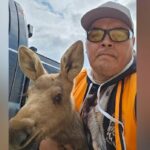 Um homem posa durante o dia para uma foto em um parque perto de uma margem do rio.