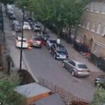 Um homem de roupas laranja é brutalmente atingido quando um carro branco se vira perigosamente na calçada