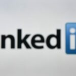 An image of a woman holding a cell phone in front of a LinkedIn logo displayed on a computer screen.
