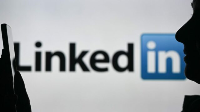 An image of a woman holding a cell phone in front of a LinkedIn logo displayed on a computer screen.