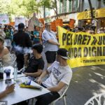 Turistas que estão amamentando bebidas em Palma de Maiorca neste fim de semana assistindo quando os demonstrantes antituristas seguram uma faixa lendo