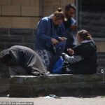 Um grupo de pessoas abraça em torno de uma mulher com um tubo (à direita), quando um homem se curva sobre uma parede coberta com o casaco, por empresas na área da Rawson Square em Bradford