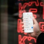 Betfair é confrontado com punição de seis dígitos depois de violar as leis de spam australianas. Uma pessoa com um smartphone branco com um aplicativo de mensagens cheio de várias mensagens de spam, com uma placa de neon vermelha que desapareceu em segundo plano.