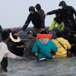Uma cerveja humana mascarada como uma marca uma bengala de açúcar e puxa uma jaqueta migrante enquanto eles tentam rastejar a bordo