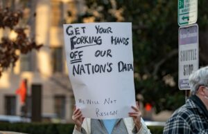 DOGE -Emprego com acesso aos dados pessoais dos americanos vazou a chave da API XAI privada a photo of a protesters in Washington DC with a sign that says "GET YOUR FORKING HANDS OFF OUR NATION'S DATA"