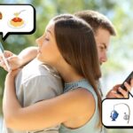 O homem fica sentado no sofá, olhando para o telefone enquanto a mulher está em segundo plano.