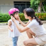 A mãe coloca um capacete rosa na cabeça da criança.