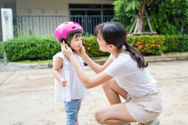 A mãe coloca um capacete rosa na cabeça da criança.