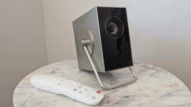 Um projetor LG Cinebeam Q 4K fica em um refrigerador, com o menu LG Webos mostrado em uma tela do Project Roon