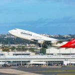 a Qantas 747 taking off from Sydney airport with the terminal building in the background.