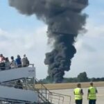 Um acidente de avião no aeroporto com uma grande pluma de fumaça preta.