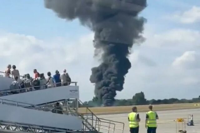 Um acidente de avião no aeroporto com uma grande pluma de fumaça preta.