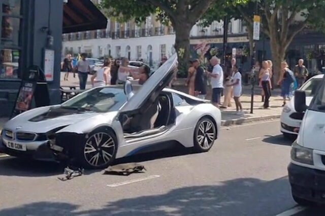 Silver BMW i8 com portas abertas após uma colisão, cercada por observadores.