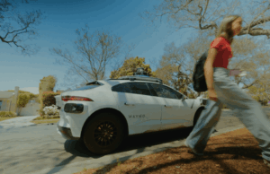 Mobilidade do TechCrunch: Tesla vem em sua era Grok e os adolescentes vêm para robotaxis A Waymo robotaxi on the street in Phoenix and a teenage girl walking away from it.