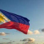 Uma foto da bandeira filipina que orgulhosamente acena um céu azul claro. As animadas cores vermelhas e amarelas da bandeira na brisa macia, com o icônico sol dourado e três estrelas amarelas decoradas sobre o cantão azul. O céu é um gradiente de cerúleo, com nuvens brancas dispersas que flutuam pacificamente para a distância. A luz solar banha a cena, enfatiza as texturas da bandeira e cria um sentimento de orgulho e serenidade nacional.