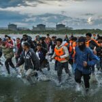Os migrantes correm pelo surf em Gravelines Beach, no norte da França, para embarcar em um bote de traficantes para a Grã -Bretanha no início deste mês