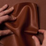 Two hands crumple Uncaged Innovations' artificial leather.