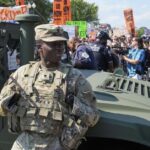 Os policiais de Washington Metropolita e os soldados da polícia militar da Região Columbia National Guardian Watch para ativistas protestam contra a aquisição federal do policiamento do policiamento do presidente do presidente Donald Trump.