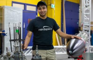 As empresas de foguetes canadenses estão correndo para lançar seus foguetes a partir de solo canadense, um mundo primeiro Quatorze homens ficam na frente de um foguete e alguns motores de foguete.