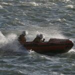 Uma mulher em um crocodilo inflável e adolescentes em um colchão de explosão teve que ser resgatado depois de 'ser derrubado para o mar' (foto: uma equipe de resgate levando os adolescentes de volta à costa)