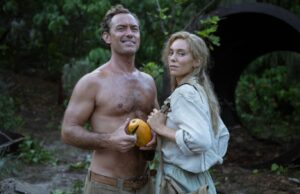 Eden Review: Ron Howards Island Drama é monótono e feio Uma mulher carrega sacos na praia, o oceano ao fundo.