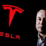 Elon Musk next to large red Tesla logo