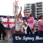 Duas mulheres detêm o padrão de St. George fora do hotel britânico para protestar Canary Wharf.