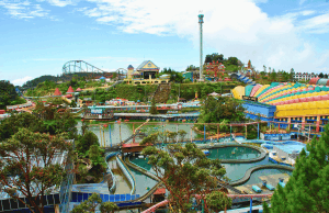 Genting Highlands Casino Chips Suspeito ‘On the Run’ Parque de diversões coloridas do lado de fora em Genting Highlands, Malásia, com montanhas -russas, passeios de água, um lago centralmente com barcos de remo e prédios animados sob um céu azul claro. Genting Highlands Casino Chips Suspeito 'On the Run'