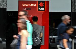 Milhões de um tapa com corte rude de taxa de efeito colateral RBA Um homem usa um caixa eletrônico NAB quando um pedestre passa.