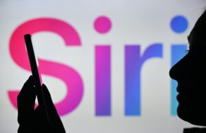 O novo Siri da Apple pode permitir que os usuários operem aplicativos que usam apenas voz An image of a woman holding a cell phone in front of the Siri logo displayed on a computer screen.