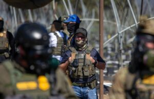 Abaixo da tecnologia que alimenta a supressão de expulsão do gelo A US Immigration and Customs Enforcement agent watches as Customs and Border Protection officers hold the line against protestors who responded to a Federal Immigration raid at Glass House Farms in Camarillo, California, July 10, 2025.