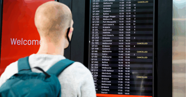 Um viajante olha para um quadro de aeroporto mostrando vários voos cancelados.