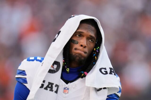 Ceedee Lamb em uma camisa branca do Dallas Cowboys com uma toalha sobre a cabeça, caminhando pela linha lateral durante um jogo.