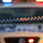 Fita de polícia em primeiro plano com um carro da polícia com as luzes acesas em segundo plano