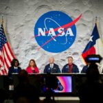 Um painel de seis pessoas se senta no palco em um evento da NASA, emoldurado pelo logotipo da NASA em um cenário da lua, com bandeiras dos EUA e do Texas ao lado deles.