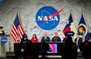 Especialistas analisam o objetivo de Artemis II Um painel de seis pessoas se senta no palco em um evento da NASA, emoldurado pelo logotipo da NASA em um cenário da lua, com bandeiras dos EUA e do Texas ao lado deles.