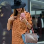 Diane Batoukina usa óculos de sol pretos, uma camiseta preta, um casaco de couro marrom marrom escuro, um cinto pequeno de couro brilhante e preto de couro de grão de grão de Hermes, calças grandes pretas, uma bolsa preta de couro brilhante e atemporal de Chanel, saltos de couro preto em parais, durante uma sessão de fotografia de estilo de rua.