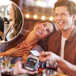Um casal sorridente em uma data de café, pagando com um cartão de crédito em um terminal.