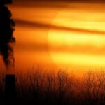 As emissões de uma usina a carvão estão em silhueta contra o sol poente