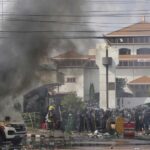 A Polícia de Riot guarda um prédio do Parlamento enquanto uma ambulância queima durante protestos em Katmandu, Nepal.