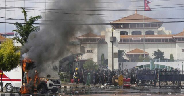 A Polícia de Riot guarda um prédio do Parlamento enquanto uma ambulância queima durante protestos em Katmandu, Nepal.